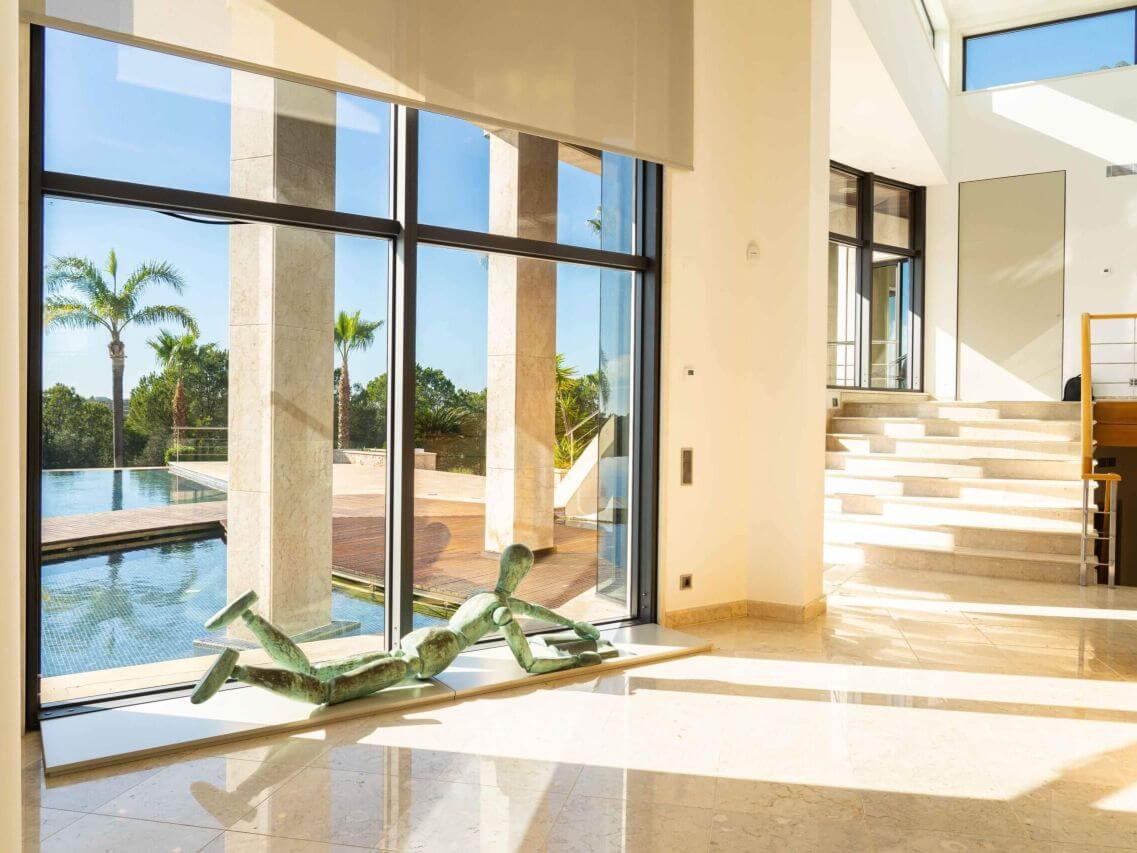 Modern luxurious interior of a Portuguese real estate property with large glass windows, natural light, and outdoor view, showcasing top-quality homes in Portugal on the QMS platform.